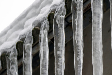 Water drips down from icicles hanging on a roof in winter weather in a snowy setting