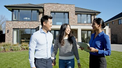 Couple embracing outside modern house with real estate agent