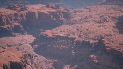 Natural beauty unfolds as sunlight casts vibrant colors on the rugged red rocks of the canyon. The vast landscape showcases unique geological formations and textures.