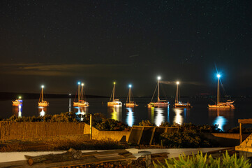 Sailboats anchored in a calm bay on the Croatian island of Silba under a star-filled night sky. Boat lights reflect on the Adriatic Sea, creating a peaceful Mediterranean island atmosphere and serene