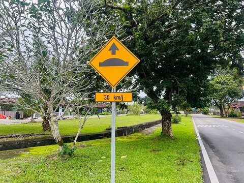 Sarawak, Malaysia - 13 January 2026: A yellow diamond-shaped traffic sign indicating a speed bump ahead, accompanied by a smaller rectangular sign specifying a speed limit of 30 km per hour.