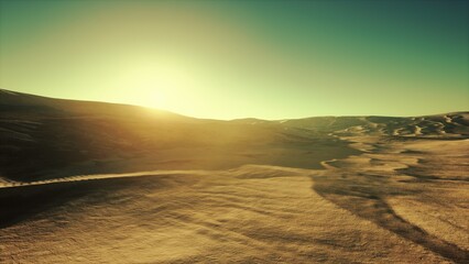Soft golden light bathes the expansive desert as the sun rises on the horizon. Shadows stretch across the undulating sand dunes creating a serene atmosphere in the early morning. © icetray