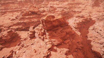 Obraz premium Majestic rock formations rise from the red sands of a desert landscape, bathed in warm light as the sun sets. Shadows stretch across the rugged surface, creating a peaceful atmosphere.