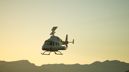 A helicopter hovers gracefully in the sky above stunning mountain ranges as the sun sets, casting...