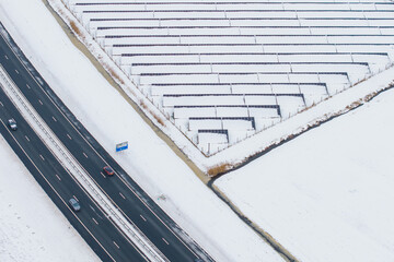 Aerial winter road alongside snow covered solar panels