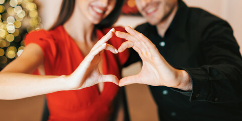 Romantic Relationship Concept. Closeup portrait of happy smiling couple making heart shape with hands, having dinner together in the evening, selective focus on fingers. Love, Connection And Bonding