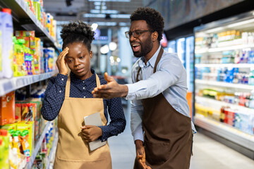 Female supermarket worker experiencing a headache and stress while a male boss is yelling and gesturing angrily at her in a grocery store, depicting workplace conflict