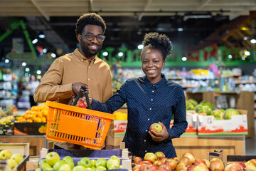 Young couple smiling as they select fresh apples from a supermarket crate during weekly grocery shopping, enjoying healthy produce and time together