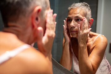 Senior woman checking her skin in bathroom mirror