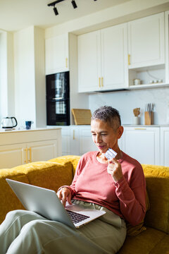 Older woman shopping online at home in modern kitchen
