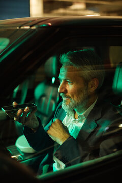 Mature businessman using voice assistant in car at night