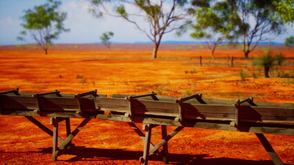 A stunning scene showcases a bright red terrain scattered with green trees. Wooden benches sit waiting for visitors, inviting them to enjoy the serene beauty of the surroundings.