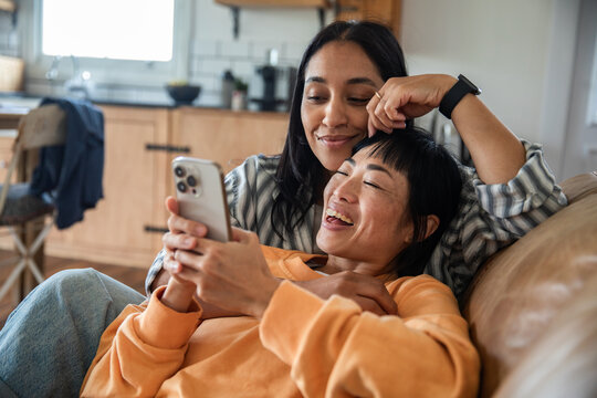 Two women relaxing on couch at home with smartphone
