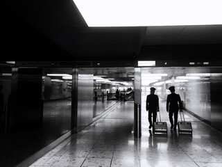 Pilots in an airport. Black and white rear view of two pilots with cases, heading towards their flight. 
