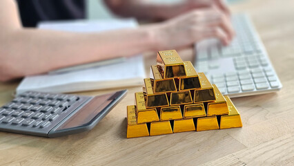 Person analyzing data with gold bars and calculator on wooden desk in office