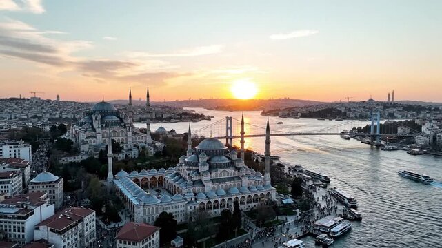 Sunset over a coastal city with domed mosque, minarets, historic rooftops, and boats and sunset glow
