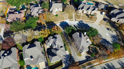 Coppell homes with landscaped yards, garages, and pools line a curved street; mix of green and red-orange trees adds seasonal texture to clean layout and suburban architecture, Texas