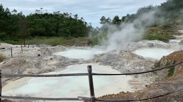 View of an active crater with boiling mud pools and dramatic plumes of sulfur smoke.