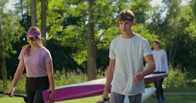 Rowers walk on the grass with kayaks, canoes and oars in their hands.