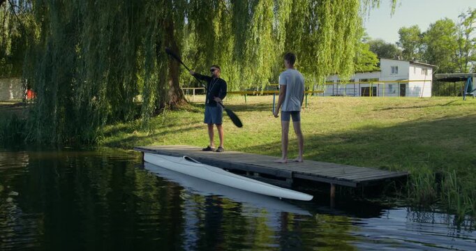 A coach shows a guy rowing technique while standing on the pier.