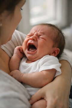 Close up view of a crying newborn baby being held, expressing infant emotions, vulnerability, and early childcare moments indoors