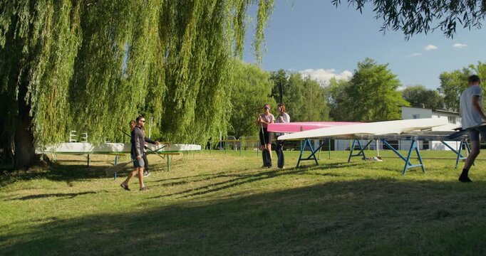 The coach gives instructions to the rowers, the guys remove the kayaks from the racks. Male and female rowers do warm-up exercises before training.