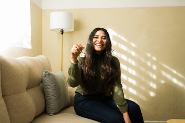 Happy woman holding new house keys, smiling at camera after buying first apartment or renting home