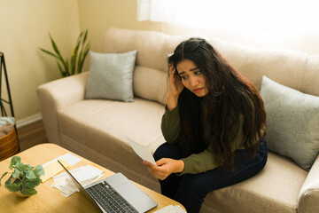Frustrated woman having financial problems at home, reading a difficult bill and feeling stressed about debt