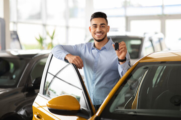 Wealthy middle-eastern businessman buying new car in luxury auto showroom, cheerful arab guy...
