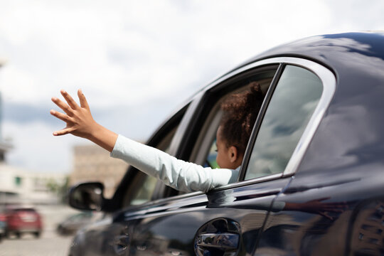 African American Kid Girl Putting Arm Out Of The Car Window Having Fun While Riding With Family In City. Summer Road Trip Adventure Concept. Back View, Selective Focus
