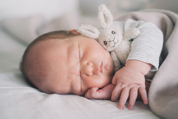 Newborn sleep at first days of life. Portrait of new born baby one week old with cute soft toy in crib in cloth background.