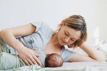 Mother breastfeeding baby. Soaked t-shirt from leaking breast milk of nursing mother. Baby eating mother's milk. Woman nursing and feeding newborn baby. Tired mother suffering postpartum depression