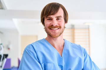 Portrait Of Smiling Male Physiotherapist In Blue Scrubs At Rehabilitation Center Healthcare Professional In Clinic Setting