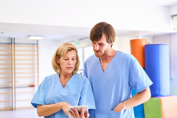 Fototapeta premium Senior Woman and Physiotherapist Using Tablet in Rehab Center for Rehabilitation and Manual Therapy Indoors Healthcare Professionals in Blue Scrubs