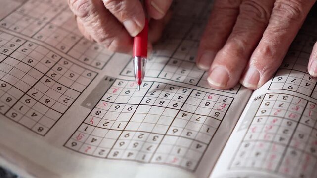 old woman, pensioner, grandmother solves Sudoku crosswords and writes numbers in a journal with a red pen. entertainment for pensioners, leisure for the elderly, brain activity, thinking,mental health