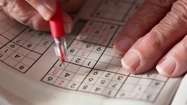 old woman, pensioner, grandmother solves Sudoku crosswords and writes numbers in a journal with a red pen. entertainment for pensioners, leisure for the elderly, brain activity, thinking,mental health