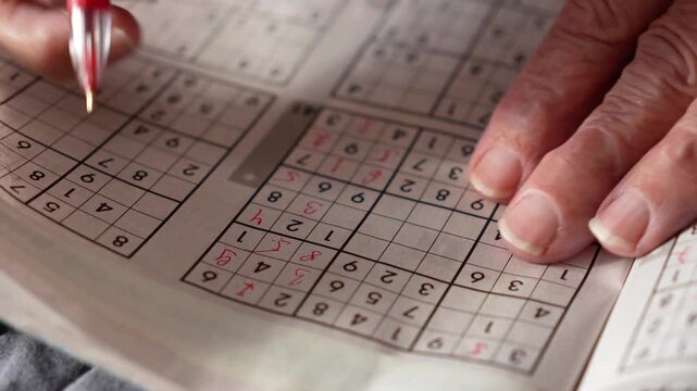 old woman, pensioner, grandmother solves Sudoku crosswords and writes numbers in a journal with a red pen. entertainment for pensioners, leisure for the elderly, brain activity, thinking,mental health