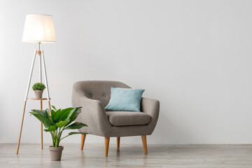 Comfort armchair with pillow, glowing lamp and potted plant on floor, on gray wall background. Home...