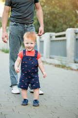 Dad and son walking outside in the summer. Happy kid boy is taking his first steps and smiling.