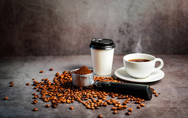 Freshly ground coffee in portafilter with roasted coffee beans and takeaway cup and coffee cup