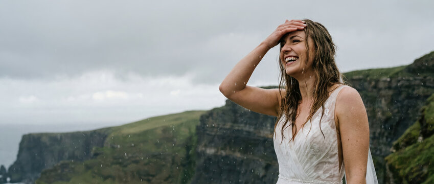 Happy woman bride on adventure elopement, smiling in rain with dramatic northern landscape. Destination wedding concept.