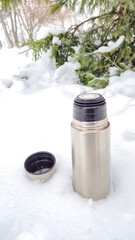 Stainless steel thermos standing upright in clean snow, symbolizing warmth, outdoor simplicity and...