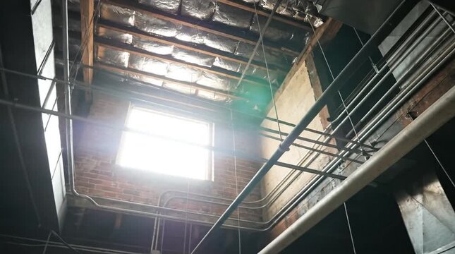 Sunlit Industrial Interior Looking Up: Bright Skylight Illuminates Exposed Wooden Beams, Insulation, Pipes, and Brick Walls in an Urban Loft or Fac...