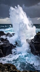 A powerful wave crashes against dark, rocky coastline under a stormy sky, creating a dramatic, dynamic waterscape