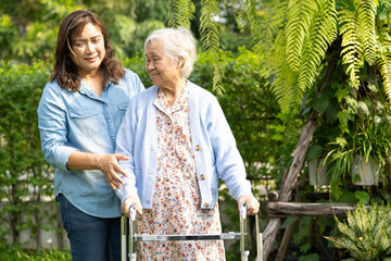 Doctor caregiver help and care Asian senior woman patient walk with walker in park at hospital.