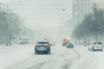 Heavy snowfall cover urban street Magdeburg car service truck move low visibility icy condition. Winter storm tram wire snow fill air traffic jam danger transport disruption harsh weather impact