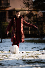 Girl rolling large snowball building snowman in winter