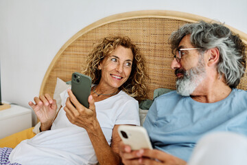 Senior middle aged couple using phone in bed in bedroom