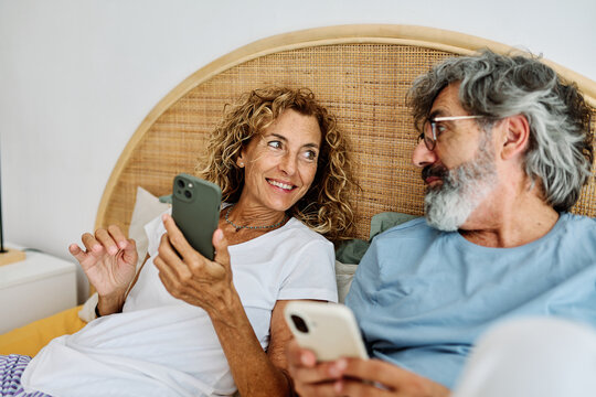 Senior middle aged couple using phone in bed in bedroom - Powered by Adobe