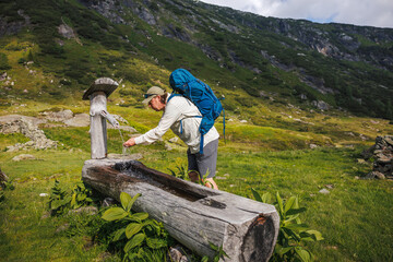 Refreshing water from mountain spring. Thirsty hiker drinking water from traditional fountain during trekking trip in Alps. Natural water source